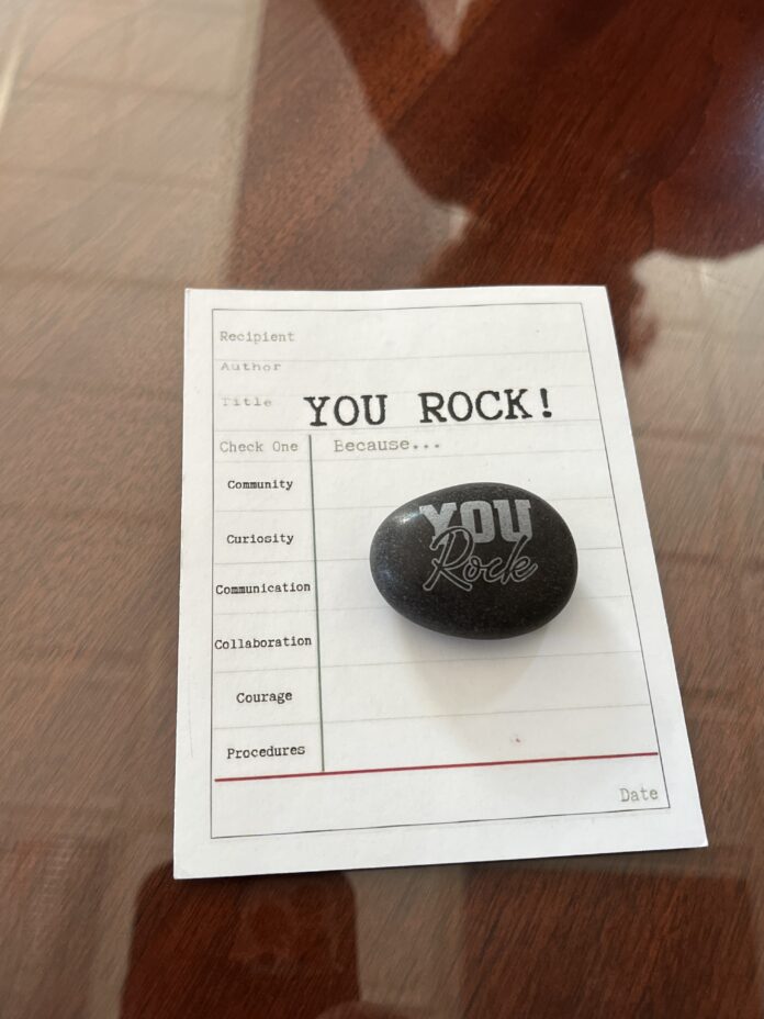 A rock with You Rock printed on the front sitting on top of a form that adorns the same writing.